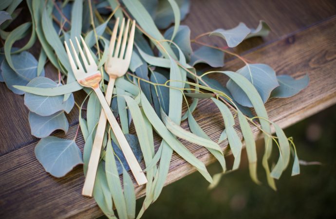 Two crossed gold forks with natural centerpiece on wooden table