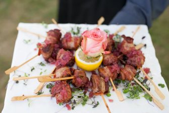 Server holding plate with bacon-wrapped appetizers and flower garnish