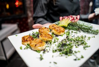 Server offering plate of single serve appetizers on bed of greens