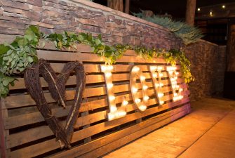 Illuminated letters spelling "love" next to a wooden, woven heart on large planks of wood