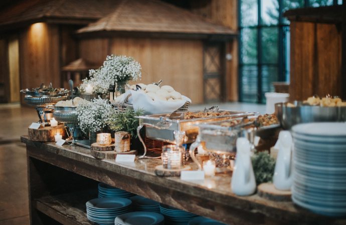 Large, wooden buffet with fresh rolls and meat trays decorated with tree stumps and white flowers