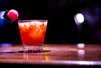 Red specialty cocktail with fruit garnish on dark bar top