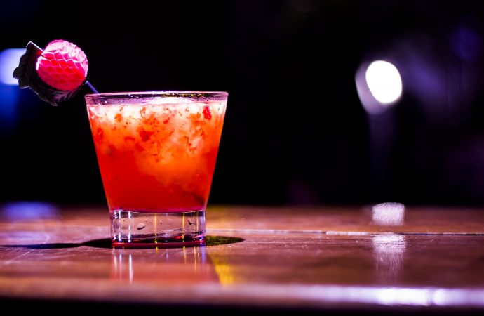 Red specialty cocktail with fruit garnish on dark bar top