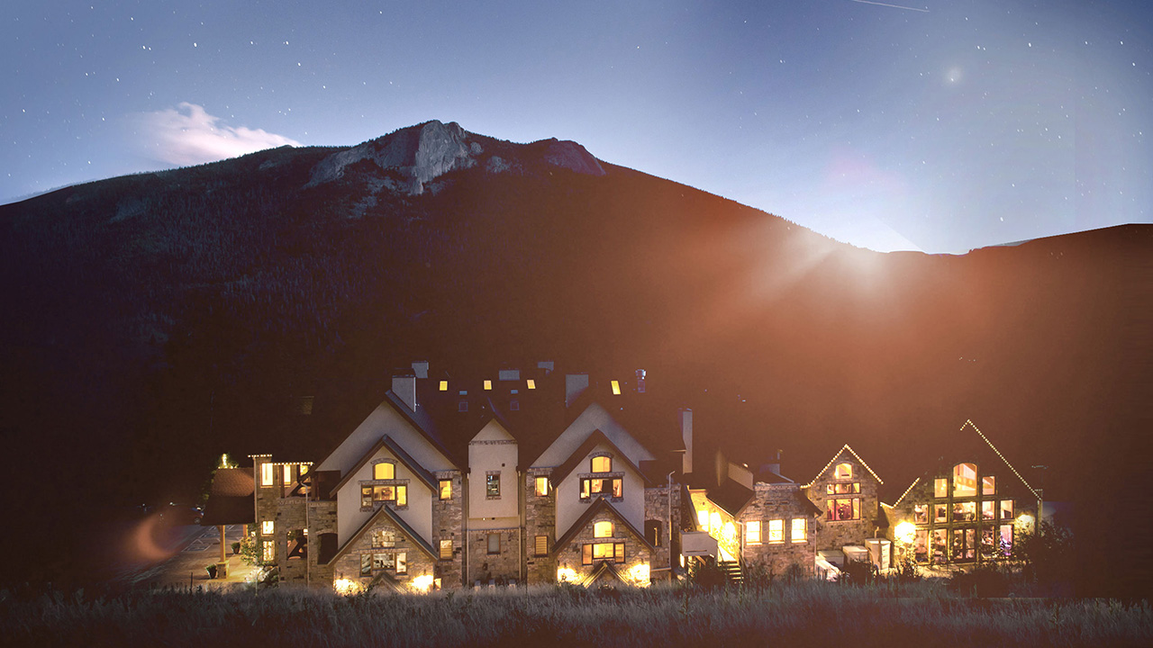 Aerial view of large mountain chateau flanked by sunset over mountain range