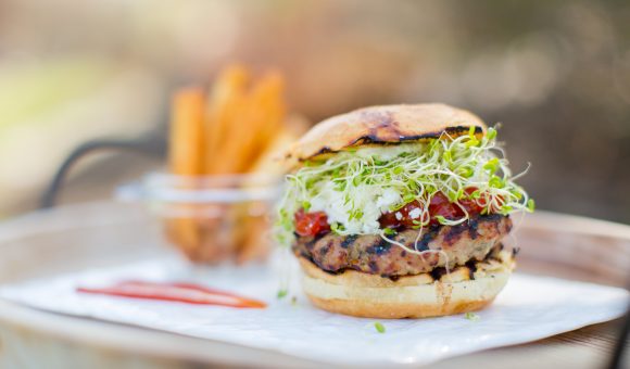 close up of burger with sprouts, fries in background