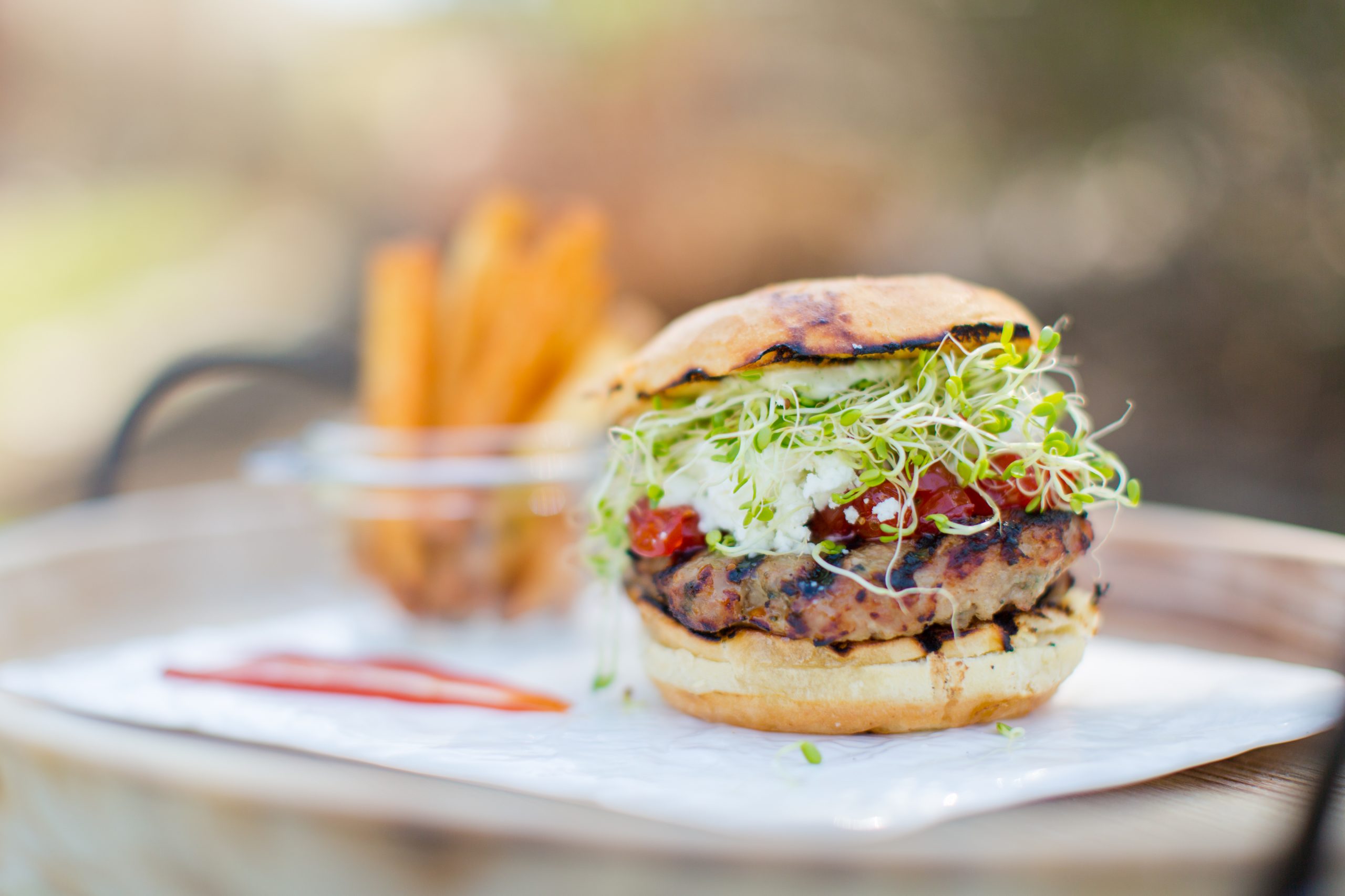 close up of burger with sprouts, fries in background